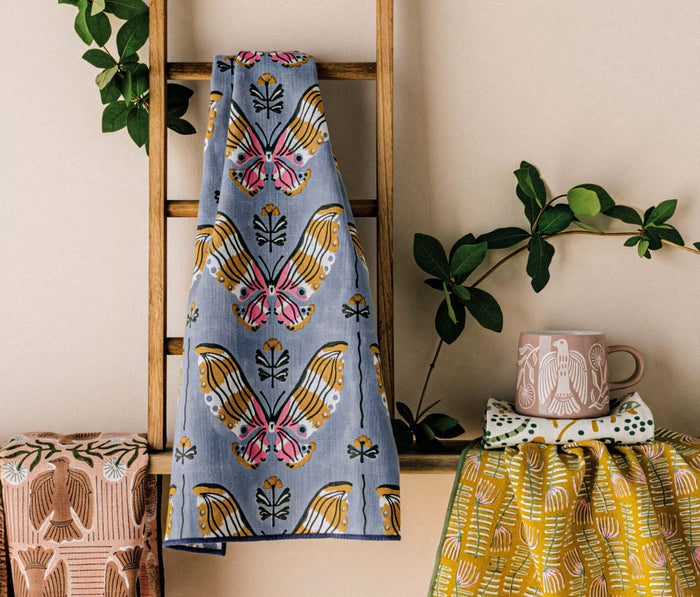 Butterfly patterned towel hanging on a wooden ladder with decorative items and plants.