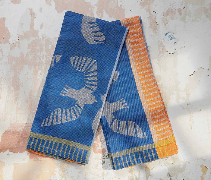 Two blue dishtowels with bird patterns on a textured beige background