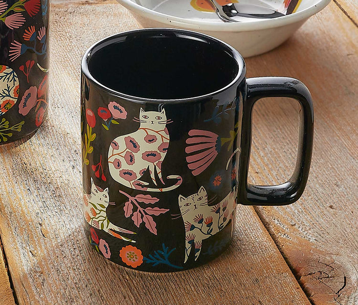 Black mug with cat and floral design on a wooden surface