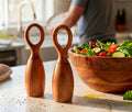 Wooden salt and pepper shakers on a kitchen counter with a salad in the background.
