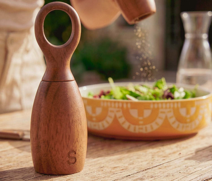 Wooden salt shaker on a wooden table with a bowl of salad in the background
