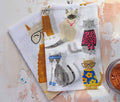 Two kitchen towels with cat illustrations on a textured surface - Lollygag