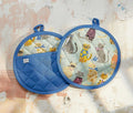 Two quilted pot holders with cat patterns on a textured surface - lollygag