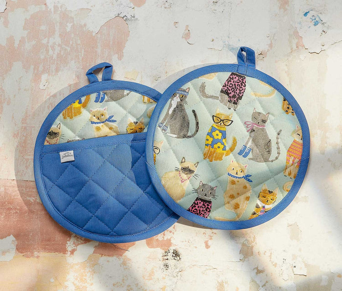 Two quilted pot holders with cat patterns on a textured surface - lollygag