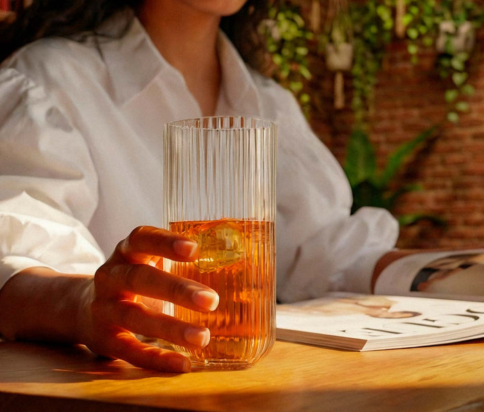 woman holding a textured glass with iced tea on a wooden table with a blurred background