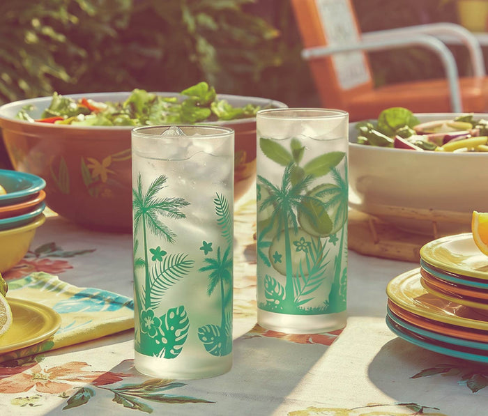 Tropical-themed glasses on a table with salad bowls and plates outdoors - Lollygag