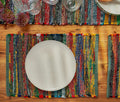 Colorful woven placemat with a white plate on a wooden table - Lollyfaf