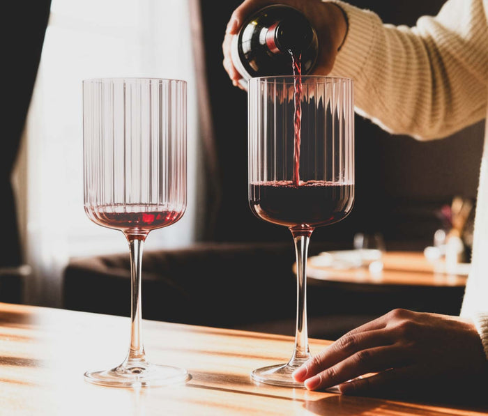 mauve pink  large wine fluted glass with a person puring red wine into it