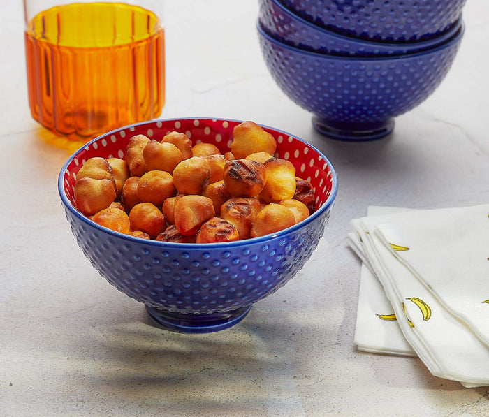 Blue textured bowl filled with pretzels on a light surface with colorful glasses and napkins.