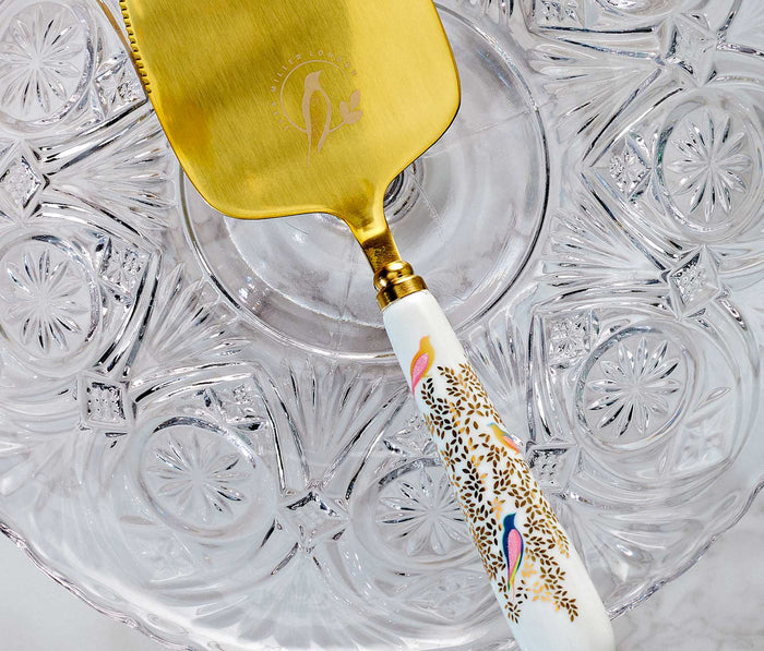 Gold-handled cake server with decorative handle on a glass plate