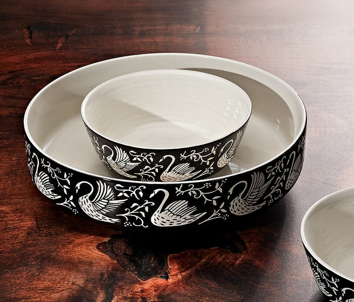 A set of nested ceramic bowls with a black and white swan and floral pattern, displayed on a dark wooden table - Lollygag