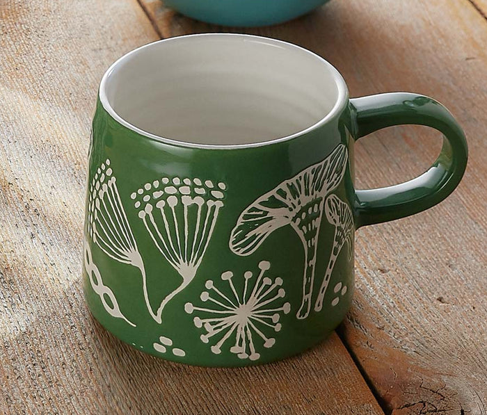 Close-up of green ceramic mug featuring embossed botanical fern and mushroom pattern